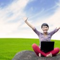 Young woman with laptop outside with arms raised