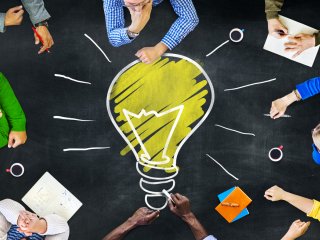 Group of people sitting around drawing of large light bulb